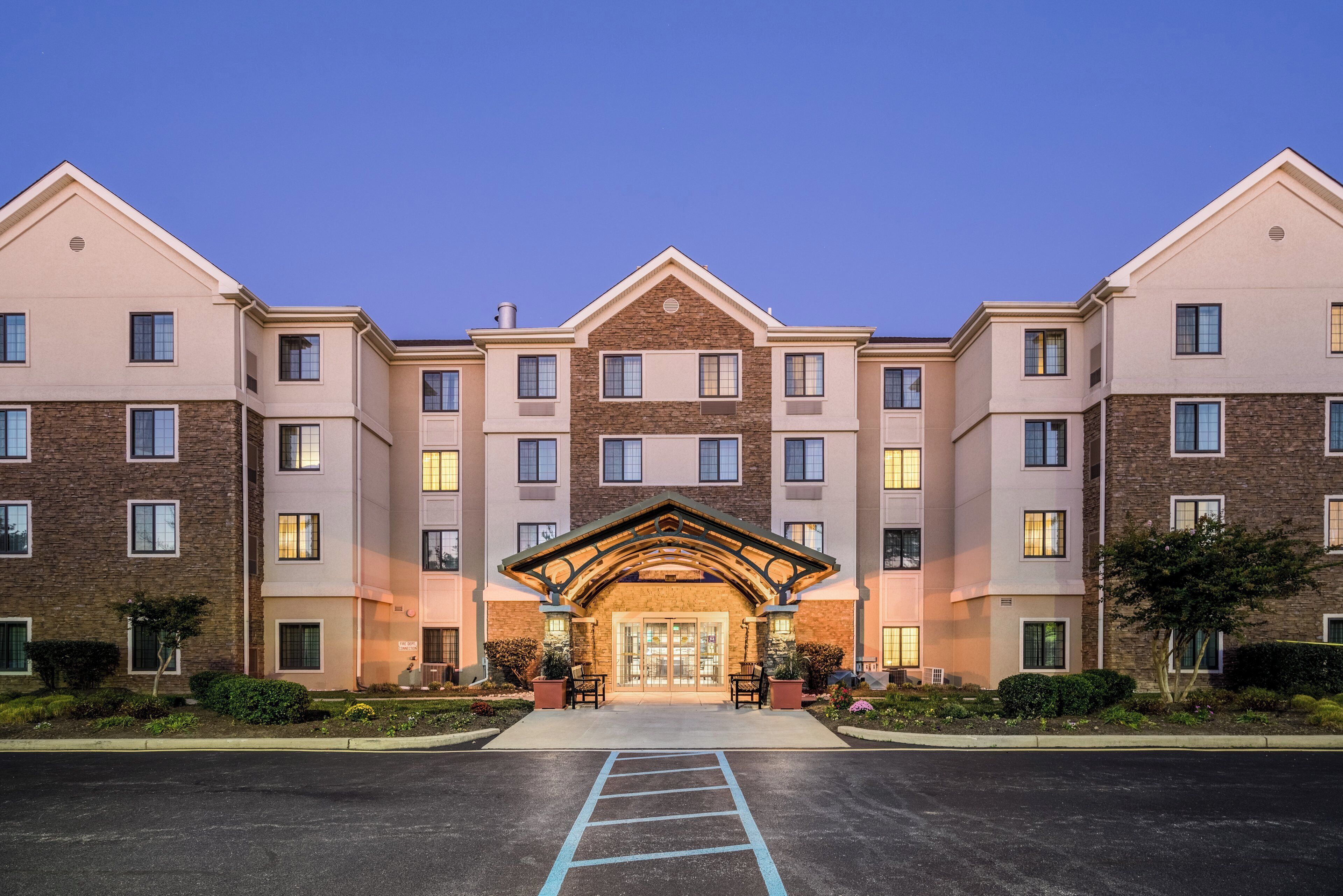 A multi-story hotel with a central entrance, a covered waiting area, and a parking lot.