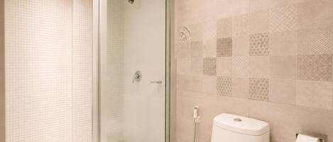 A bathroom with a glass-enclosed shower, a toilet, and a patterned tile wall.