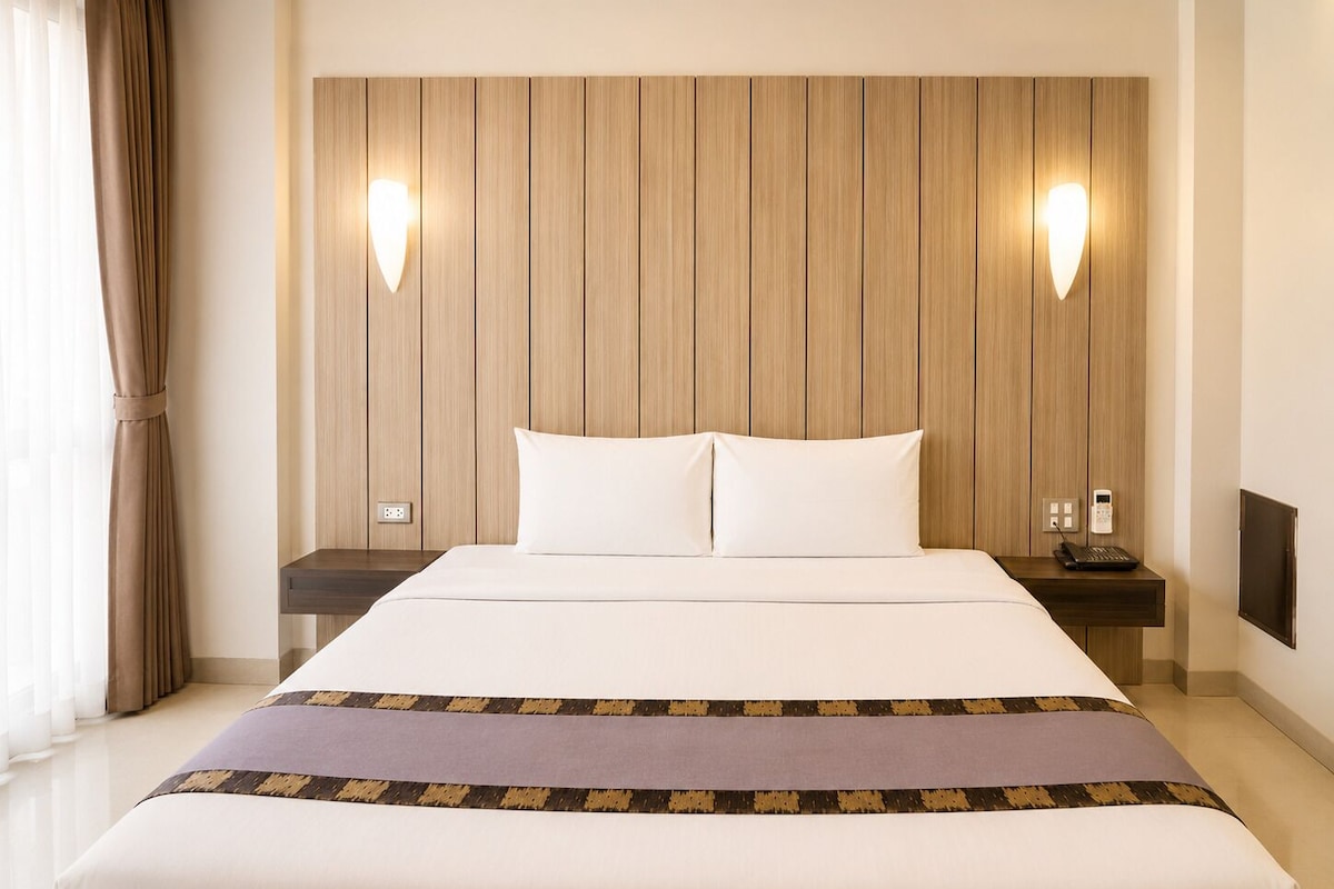 A hotel room with a large bed, two bedside tables, a wall-mounted phone, and a window with curtains.