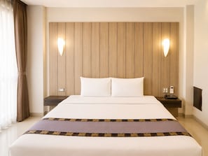 Een hotelkamer met een groot bed, twee nachtkastjes, een telefoon aan de muur en een raam met gordijnen.