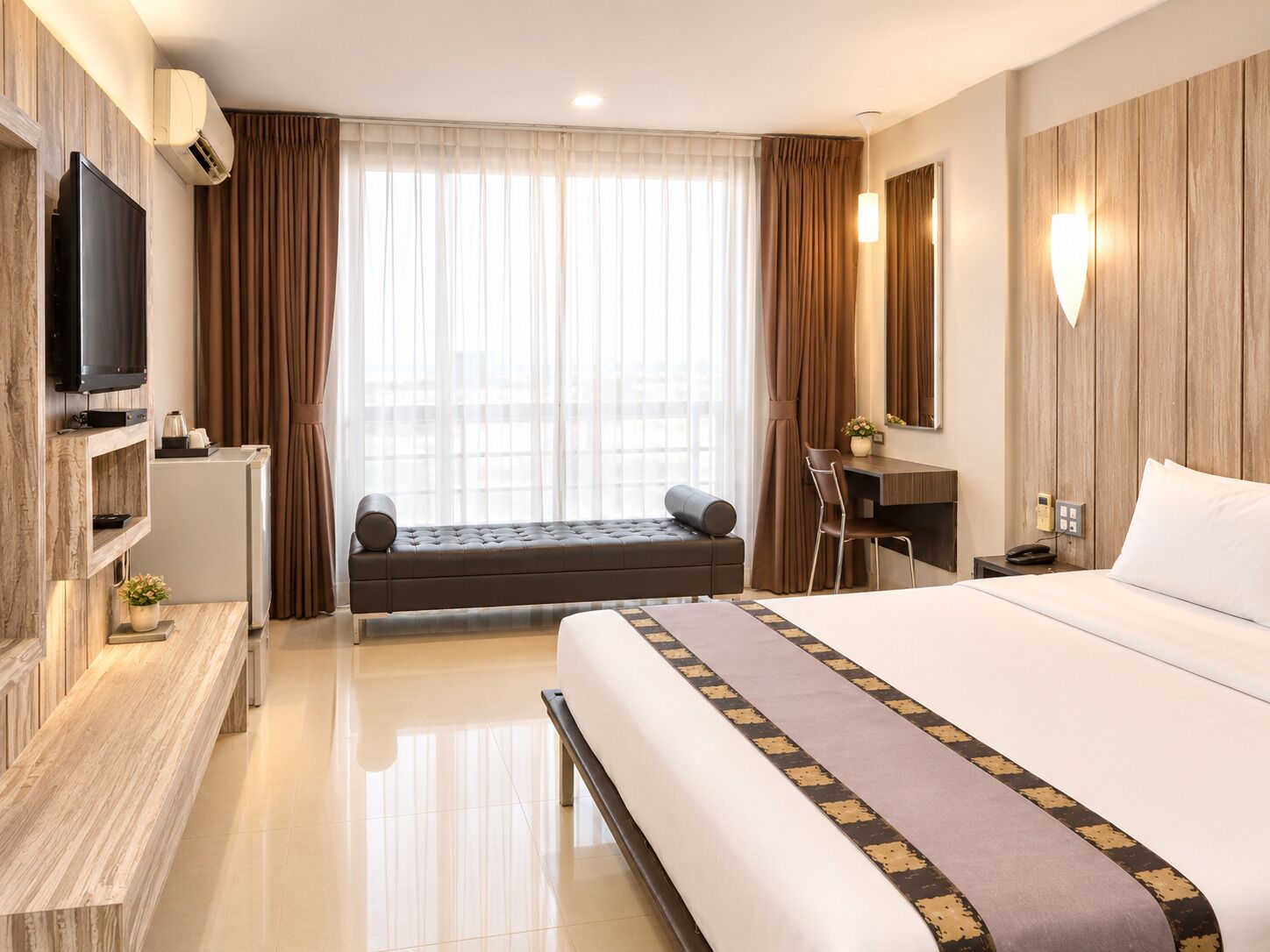 Habitación de hotel con cama, escritorio, televisor y vistas a la ciudad a través de amplias ventanas.