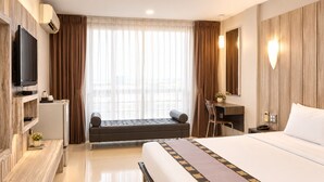 A hotel room with a bed, a desk, a television, and a view of the city through large windows. - Swana Bangkok Hotel (Bangkok)
