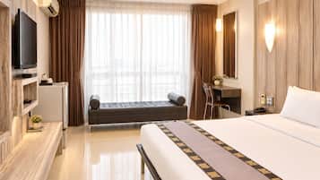 Habitación de hotel con cama, escritorio, televisor y vistas a la ciudad a través de amplias ventanas.