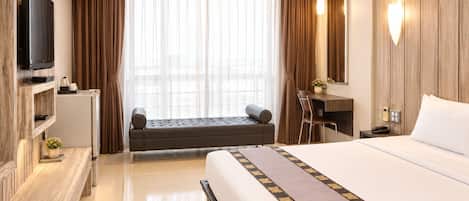 A hotel room with a bed, a desk, a television, and a view of the city through large windows.