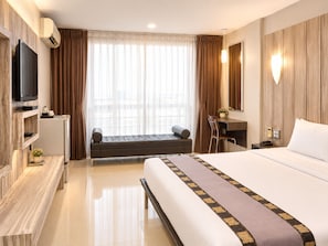 A hotel room with a bed, a desk, a television, and a view of the city through large windows.