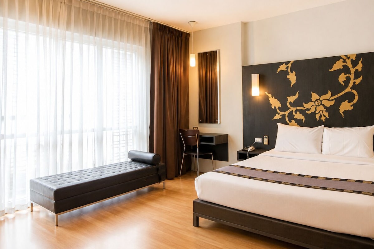 A hotel room with a bed, a desk, a chair, and a bench.