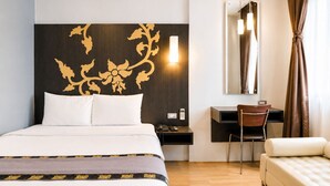 A hotel room with a bed, a desk, a chair, a sofa, a mirror, and a wall with a decorative pattern. - Swana Bangkok Hotel (Bangkok)