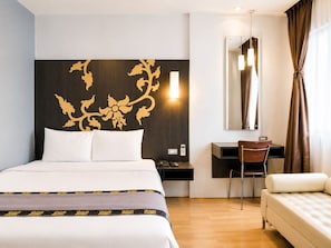 A hotel room with a bed, a desk, a chair, a sofa, a mirror, and a wall with a decorative pattern.