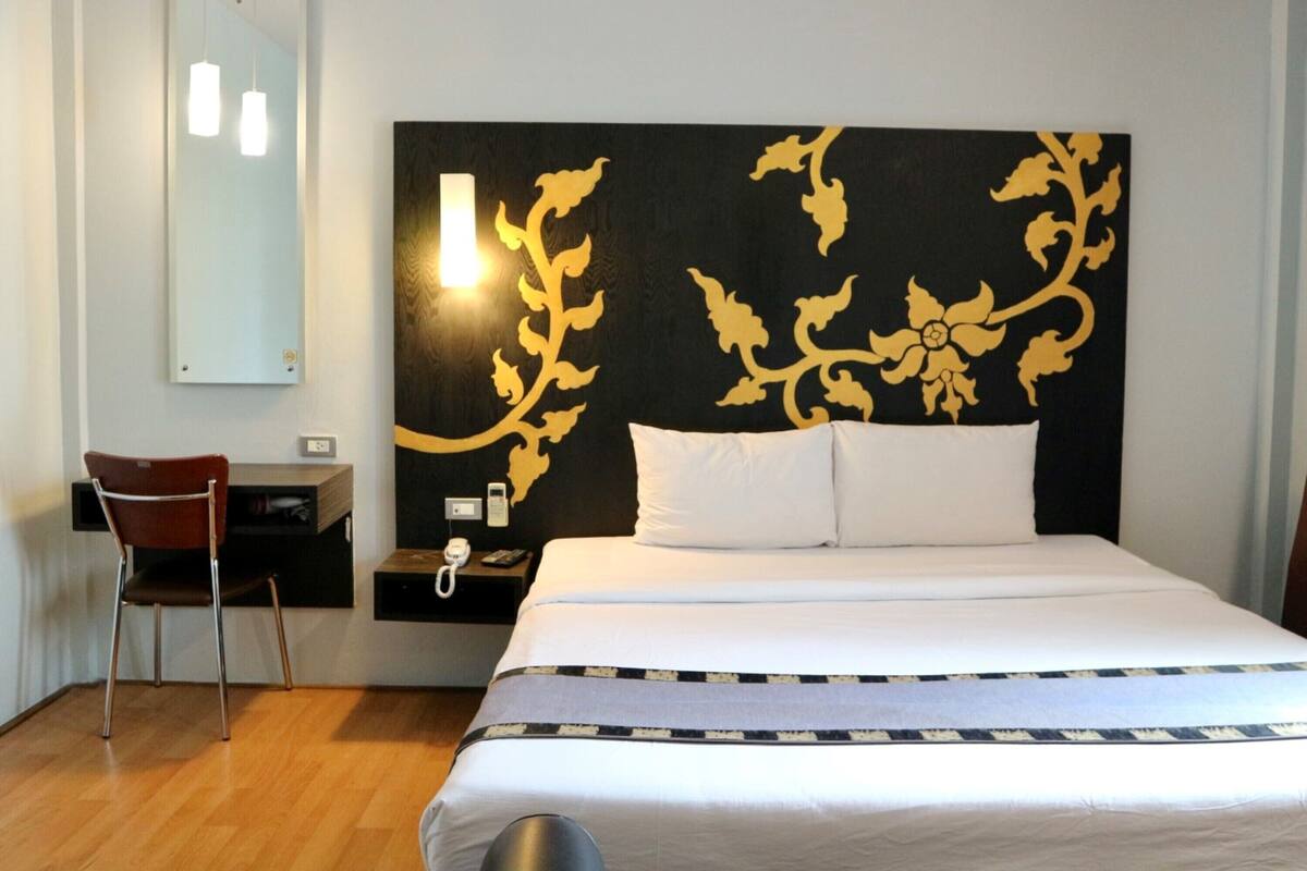 Quarto de hotel com uma cama, uma cadeira, mesa de cabeceira com telefone e espelho fixado na parede.