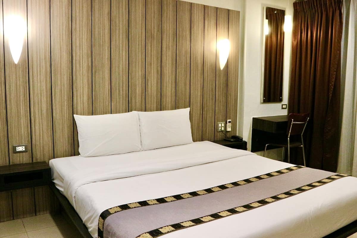 Quarto de hotel com uma cama grande, uma escrivaninha e uma cadeira. Há duas luzes na parede e um espelho sobre a escrivaninha.