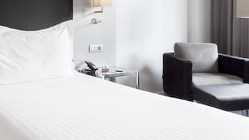 Une chambre d’hôtel comprenant un lit, une chaise, une table de chevet avec une lampe et un luminaire fixé au mur.