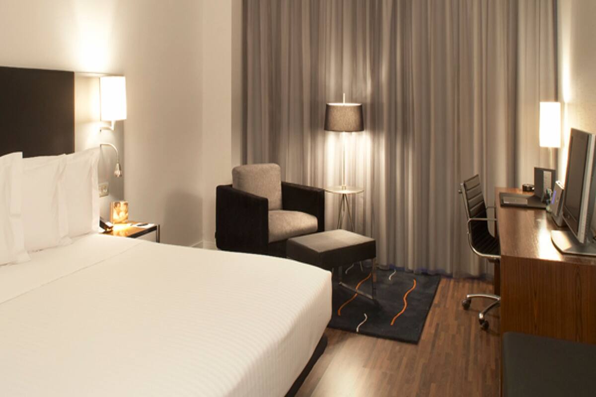 Une chambre d’hôtel avec un grand lit, un bureau avec un ordinateur, une chaise, une lampe de bureau et une fenêtre avec des rideaux.