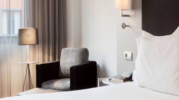 Ein Hotelzimmer mit Bett, Stuhl, Lampe und Wandleuchte.
