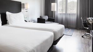 A hotel room with two beds, a desk, a chair, a lamp, and a window with curtains.
