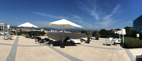 A rooftop terrace with outdoor seating, umbrellas, and a city view.