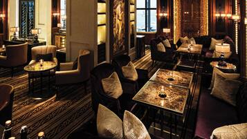 A luxurious hotel lobby with a bar, seating areas, and a large window offering a view.
