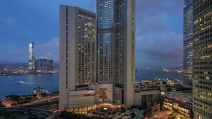 A high-rise hotel with multiple floors, a central courtyard, and a view of the city skyline and water body in the background.