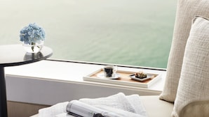 A room with a view of the sea, a table with a book, a cup, and a small plant.
