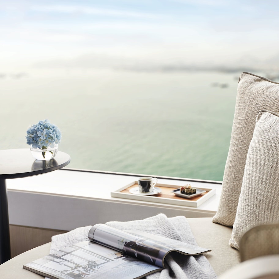 A room with a view of the sea, a table with a book, a cup, and a small plant.
