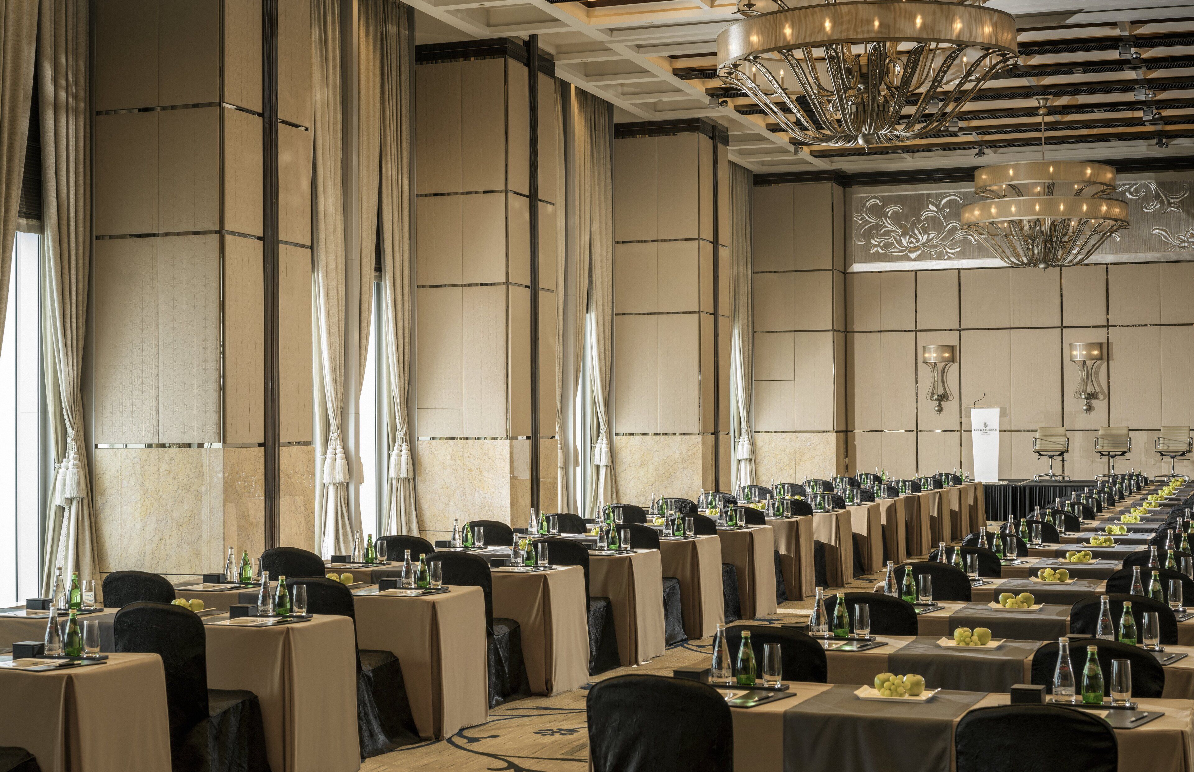 A banquet hall with long tables set for a formal event, featuring chandeliers and a high ceiling.