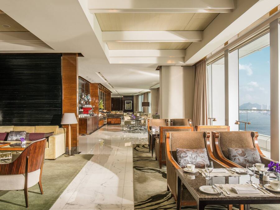 A spacious hotel lobby with a dining area, a bar, and a view of the sea.