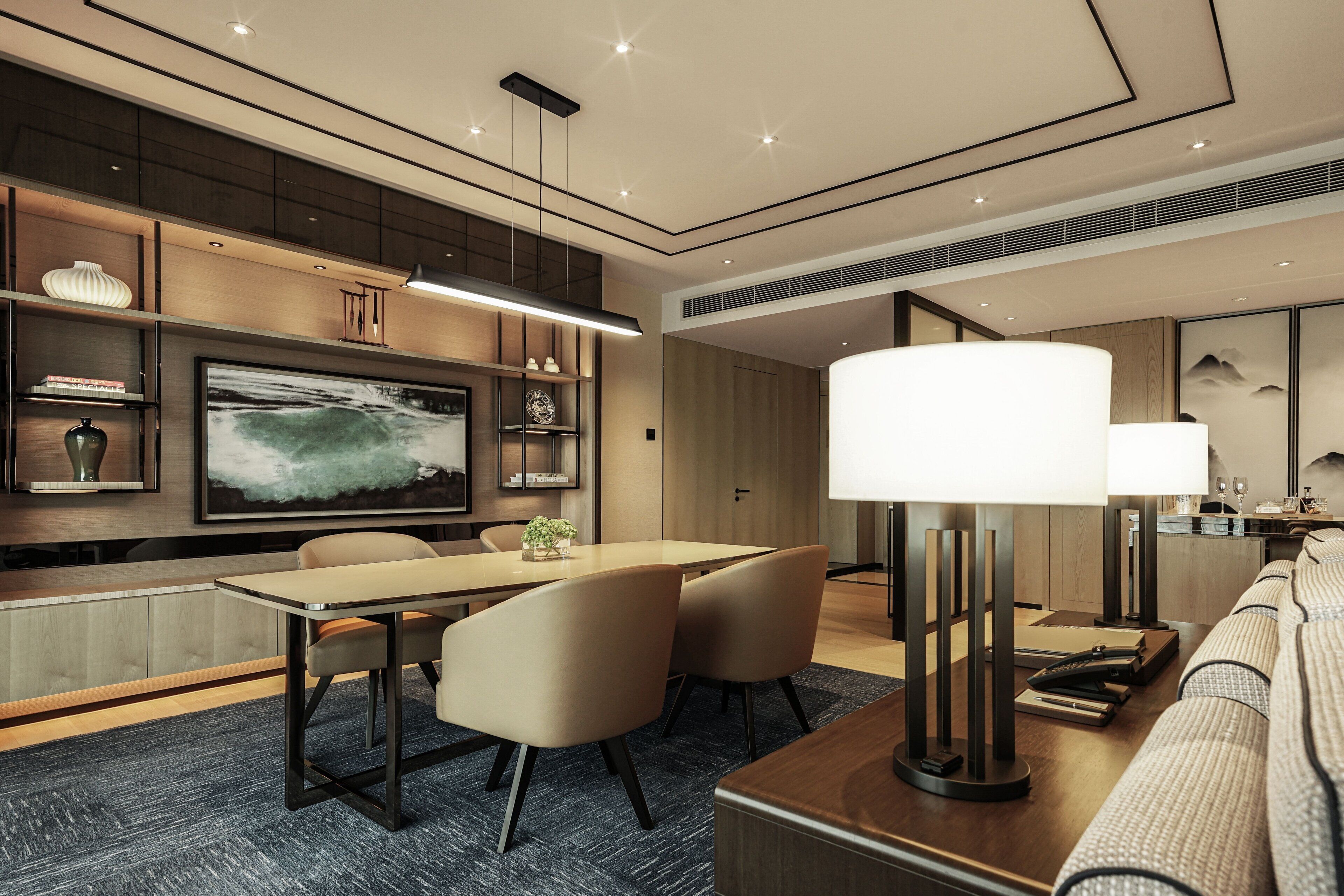 A modern hotel room with a dining area, a large flat-screen TV, and a sofa.