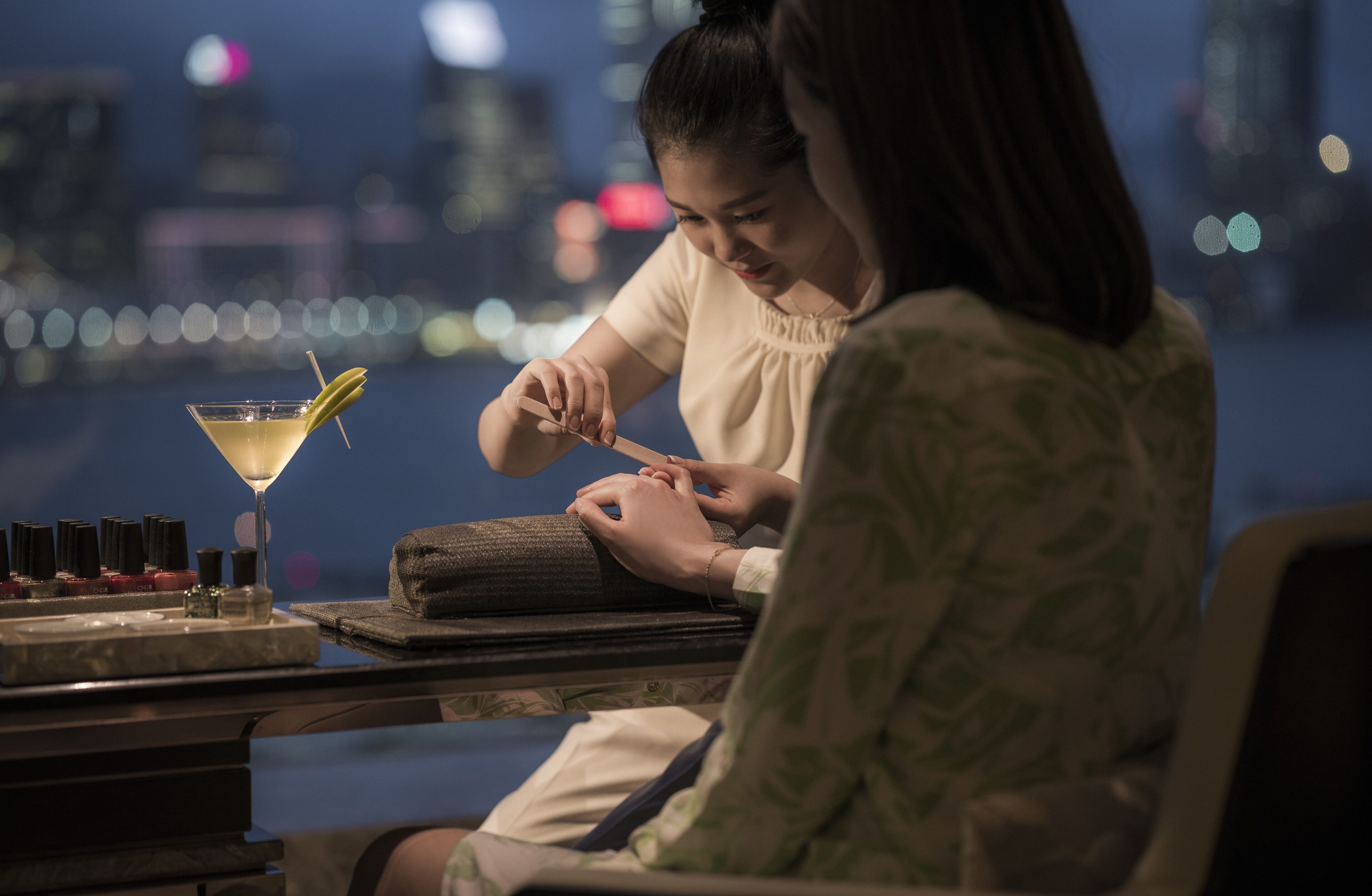 A person receiving a manicure at a bar with a cocktail on the counter.