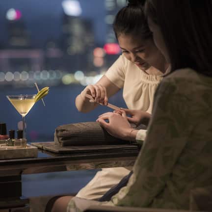A person receiving a manicure at a bar with a cocktail on the counter.