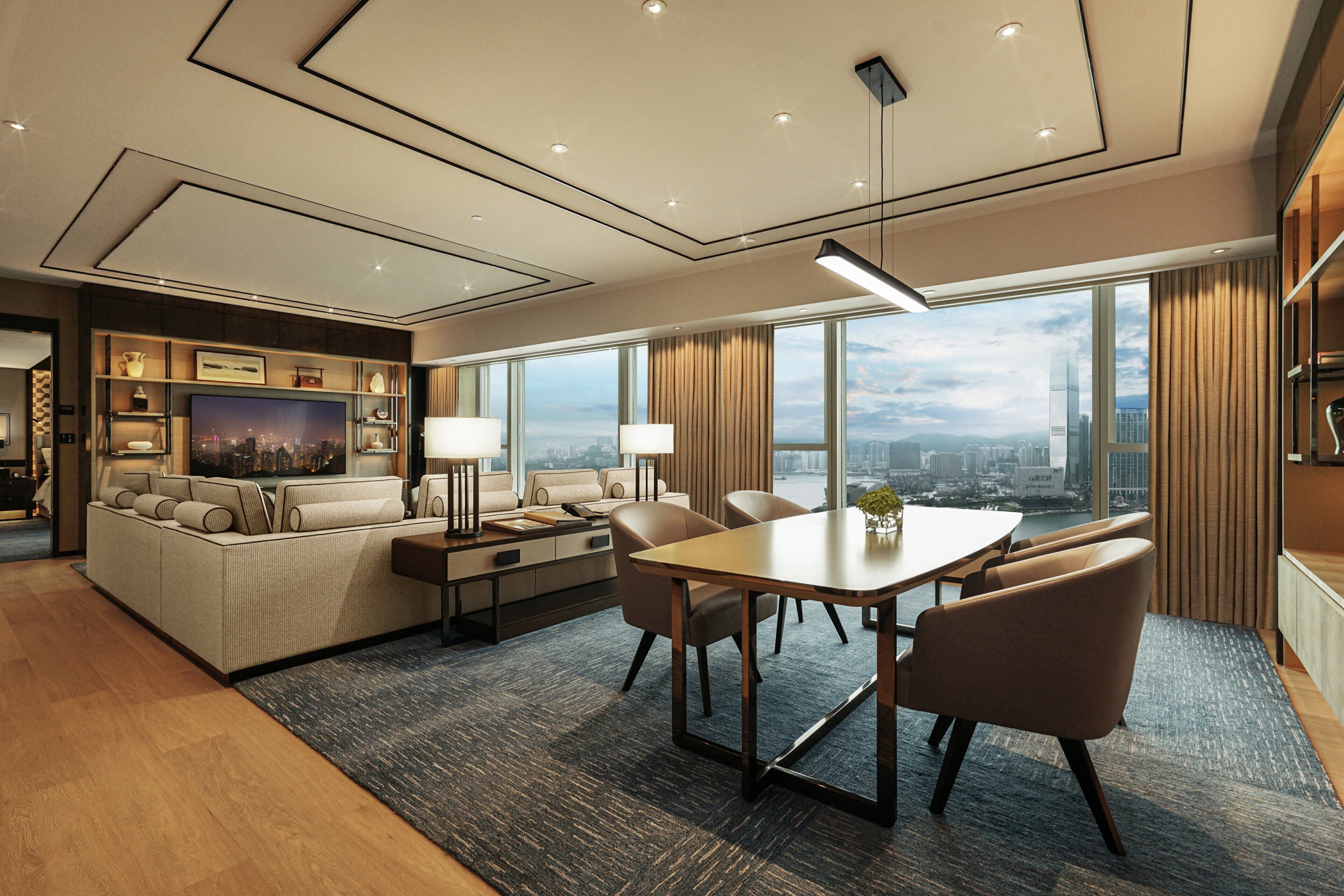 A modern hotel room with a living area, a dining table, and a large window offering a city view.