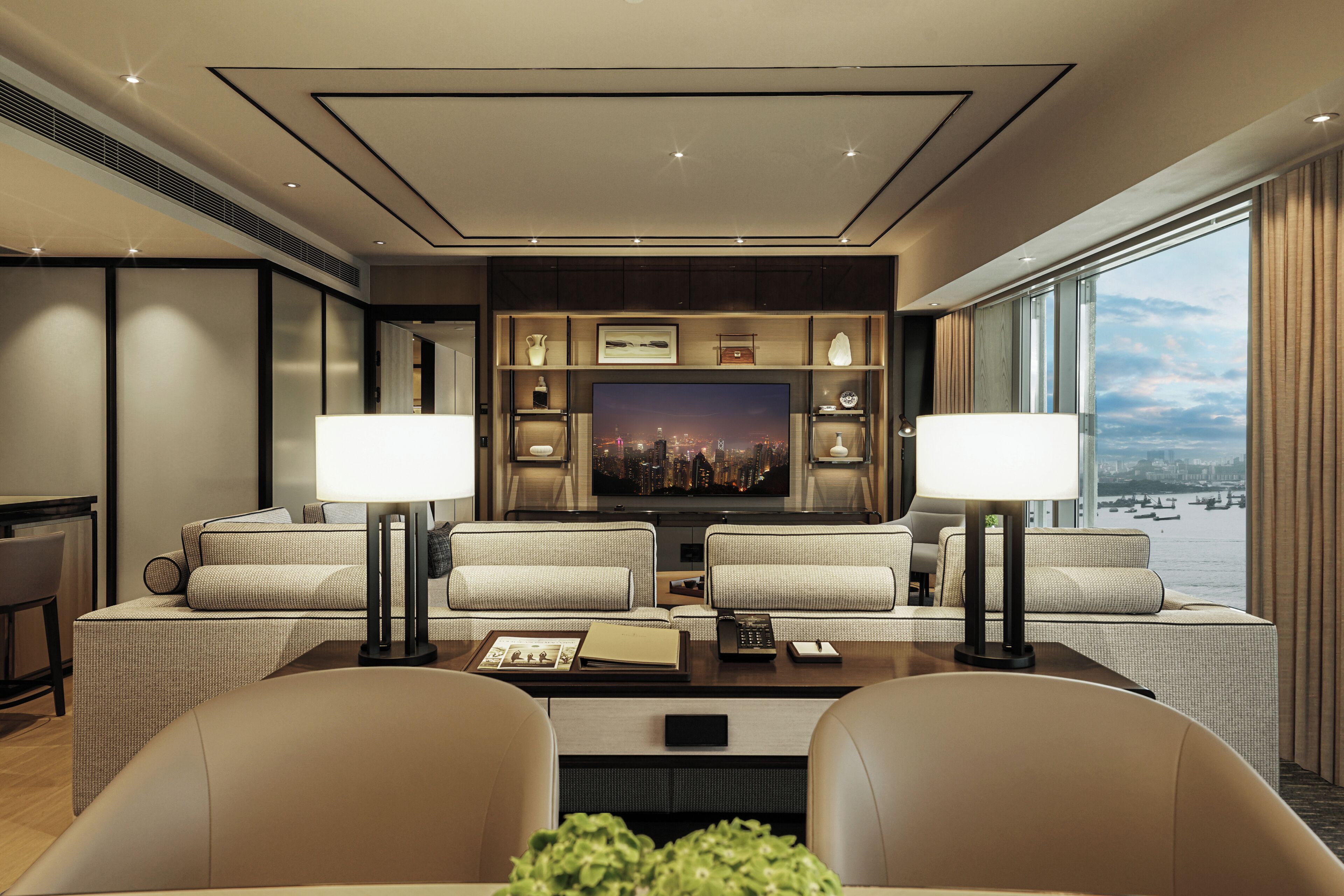 Ein modernes Wohnzimmer mit großem Flachbildfernseher, zwei Sofas, einem Couchtisch und Blick auf die Stadt durch große Fenster.