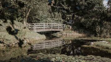 Uma ponte de madeira sobre um lago com nenúfares, rodeada por árvores e vegetação.