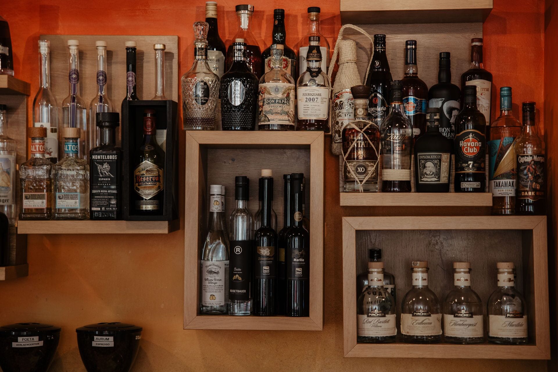 Une variété de bouteilles de spiritueux sont exposées sur des étagères, le tout adossé à un mur en bois.