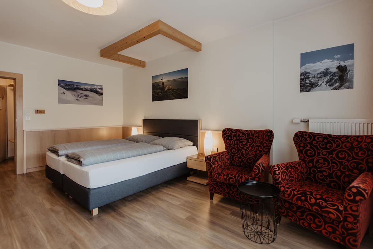 Une chambre à coucher avec un lit, une table de chevet, une chaise et une petite table. Il y a deux tableaux accrochés au mur.
