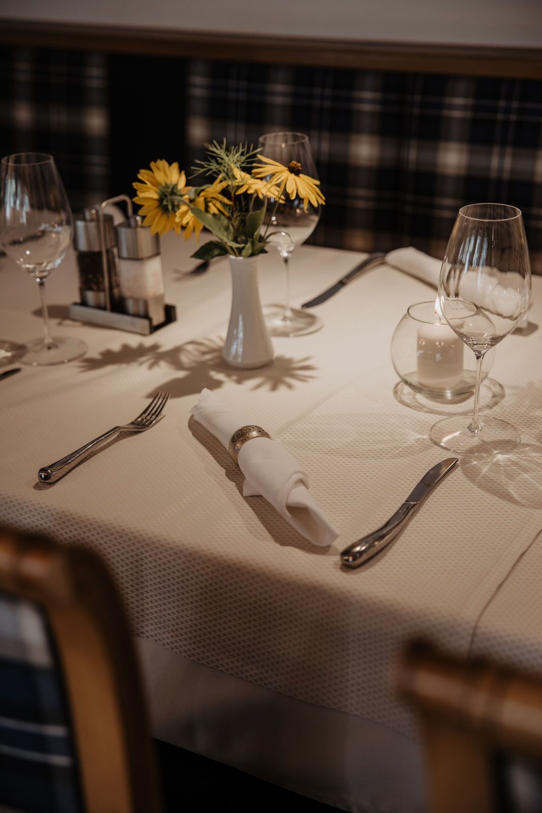 A table set for dining with a vase of yellow flowers, wine glasses, and cutlery.
