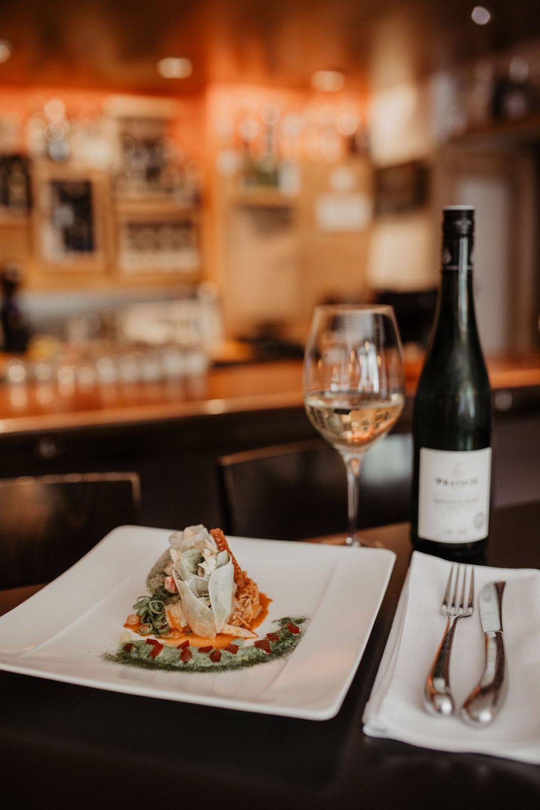 Una mesa de comedor con un plato de comida, una copa de vino y una botella.