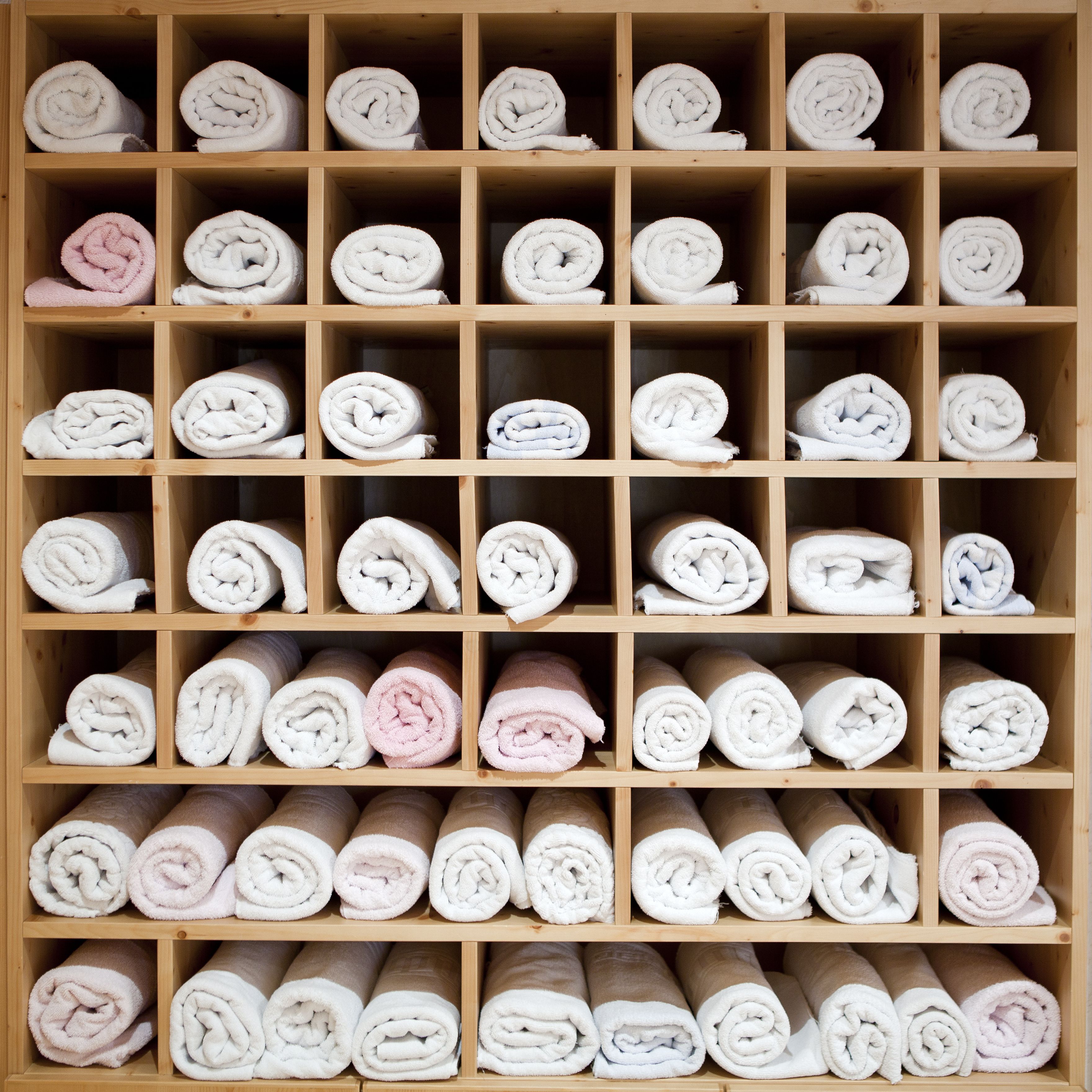 A wooden shelf with neatly rolled towels in various colors.