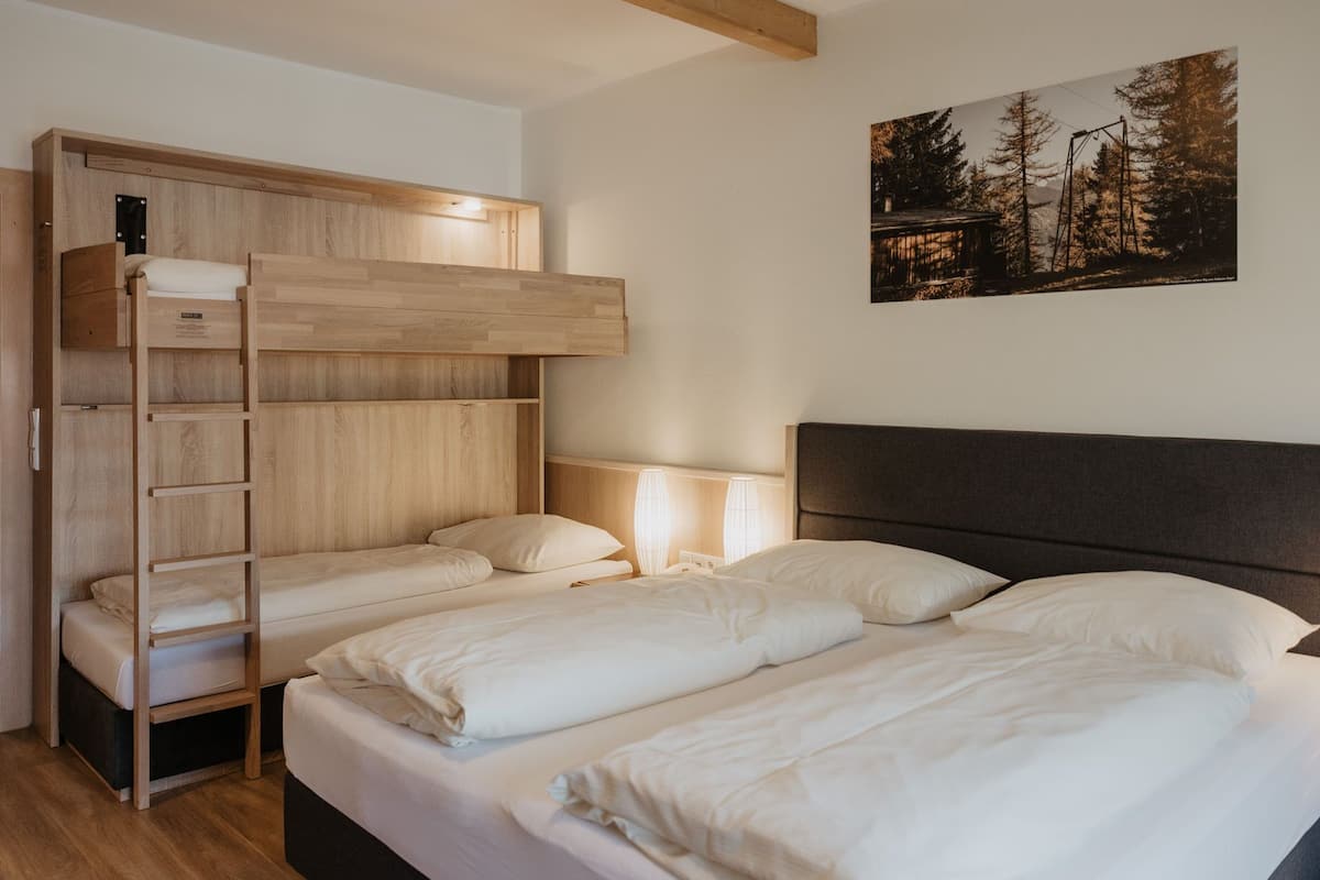 Un lit superposé avec une échelle en bois, une table de chevet avec des lampes et un lit avec une literie blanche.