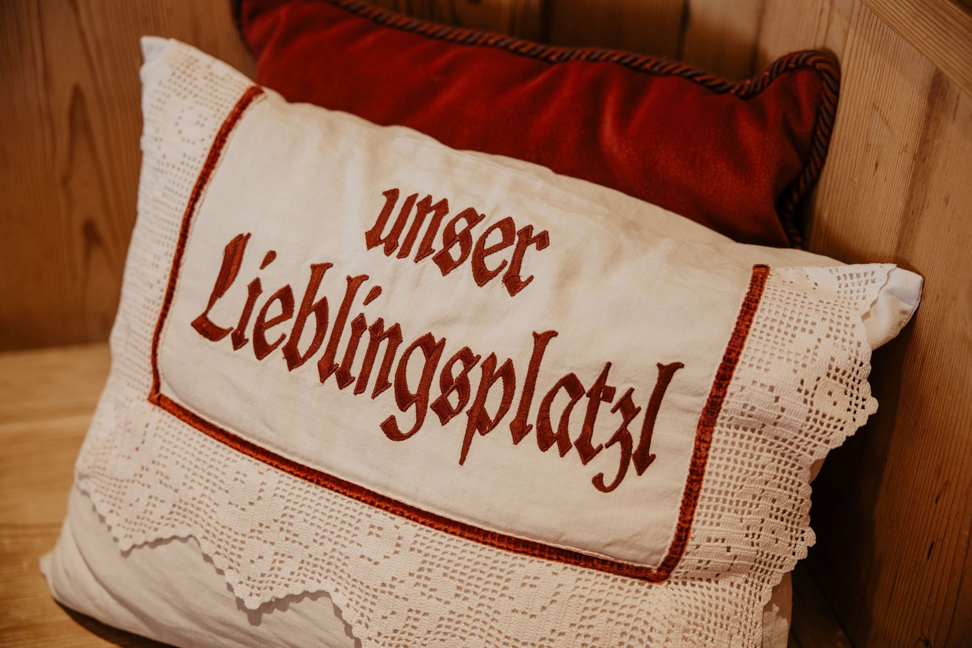 A pillow with embroidered text "Unser Lieblingsplatz" on a white fabric with a lace trim.