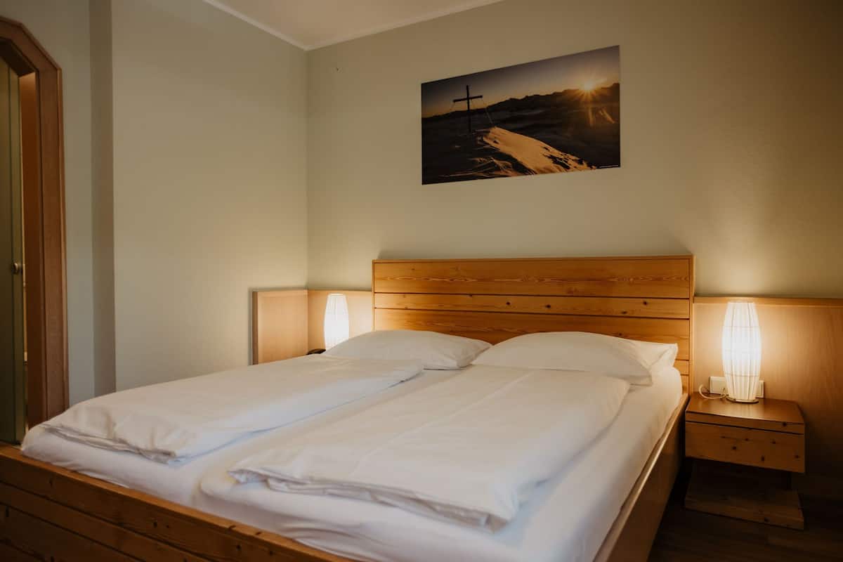 Un lit double bien fait, avec du linge de lit blanc, deux tables de chevet avec des lampes et un tableau encadré au mur.