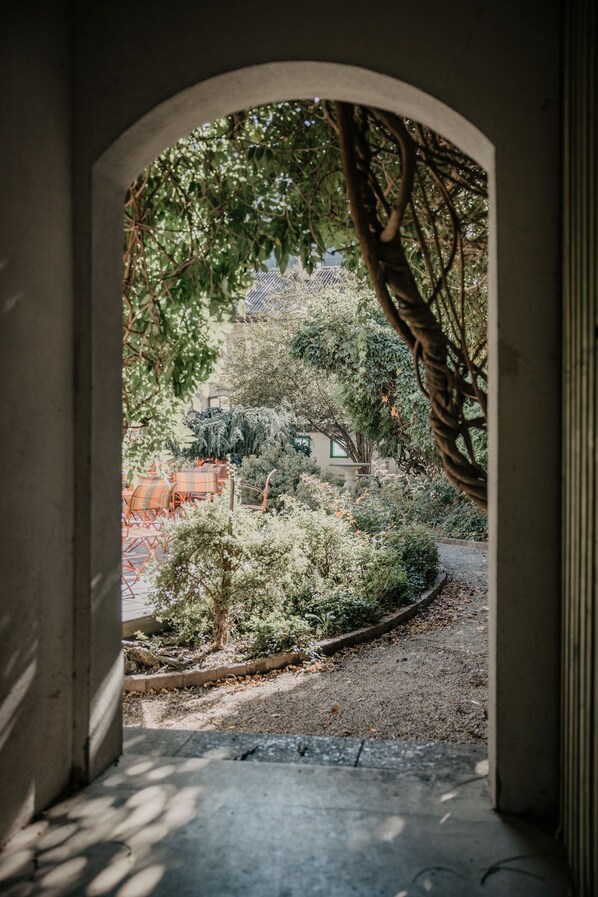 An arched doorway leading to a garden with a variety of plants and a small tree. - Parkhotel Matrei (Matrei am Brenner)