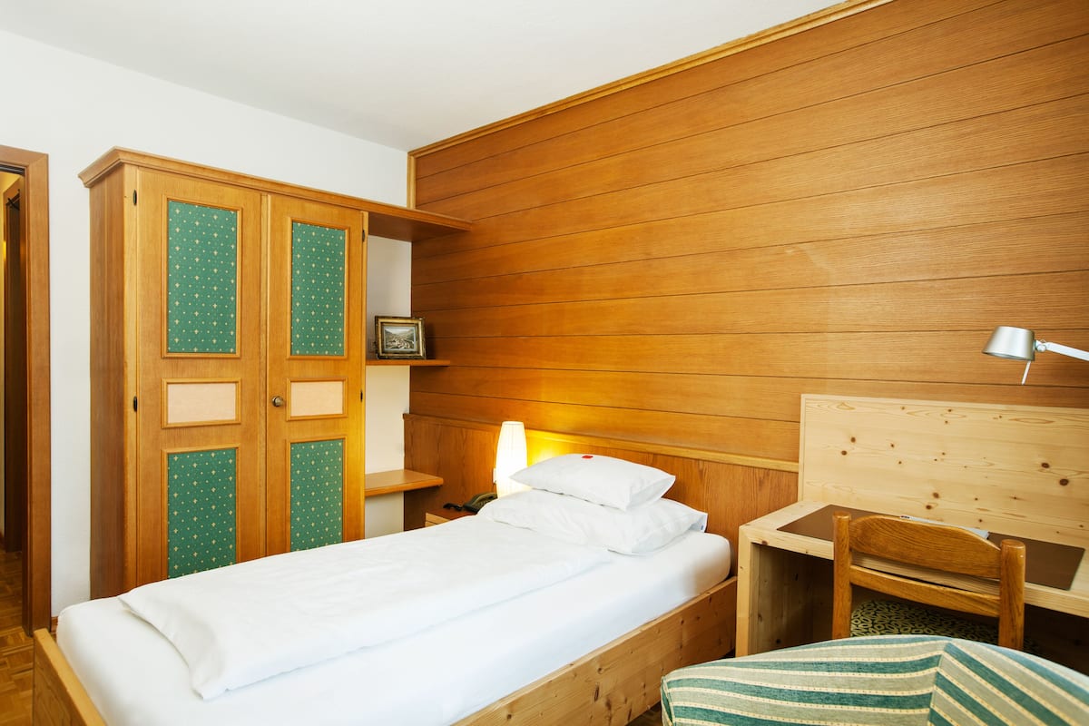 Une pièce aux murs lambrés, comprenant un lit, un bureau et une armoire.