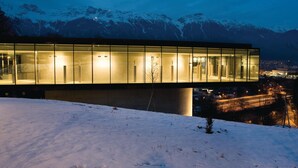Ein modernes Gebäude mit Glasfassade, eingebettet in einen verschneiten Hang mit Bergblick.