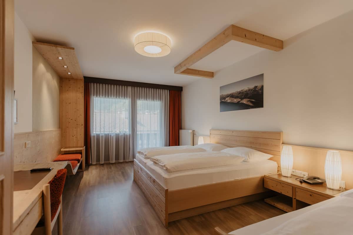 Une chambre d’hôtel avec un lit en bois, un bureau, une chaise, une table de chevet et une lampe fixée au mur.