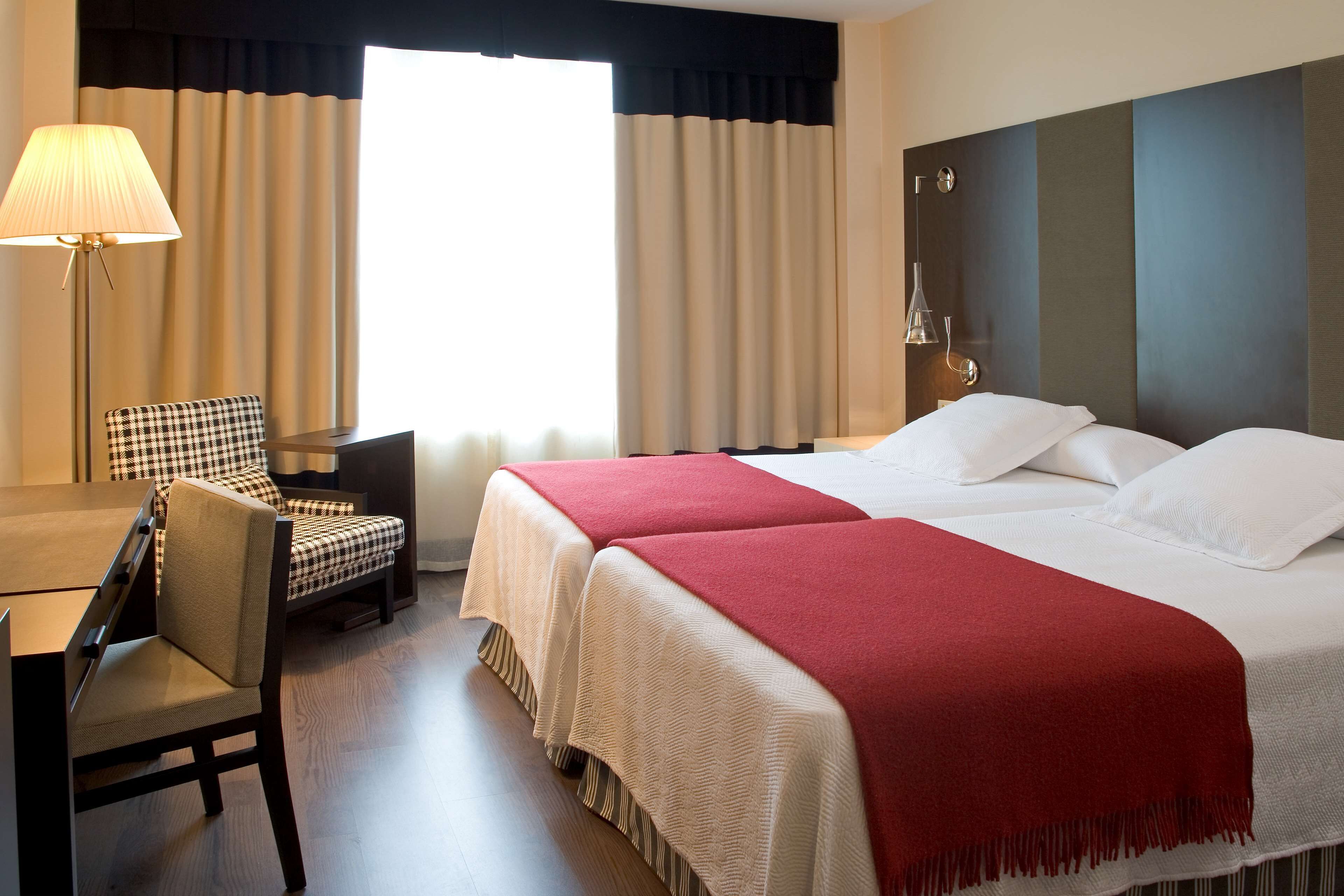 Ein Hotelzimmer mit zwei Betten, einem Schreibtisch, einem Stuhl und einer Lampe.