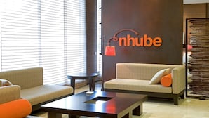A modern lobby with a sofa, armchair, and coffee table. A wall sign reads "nhube by terran adria". - NH Valladolid Bálago (Valladolid)