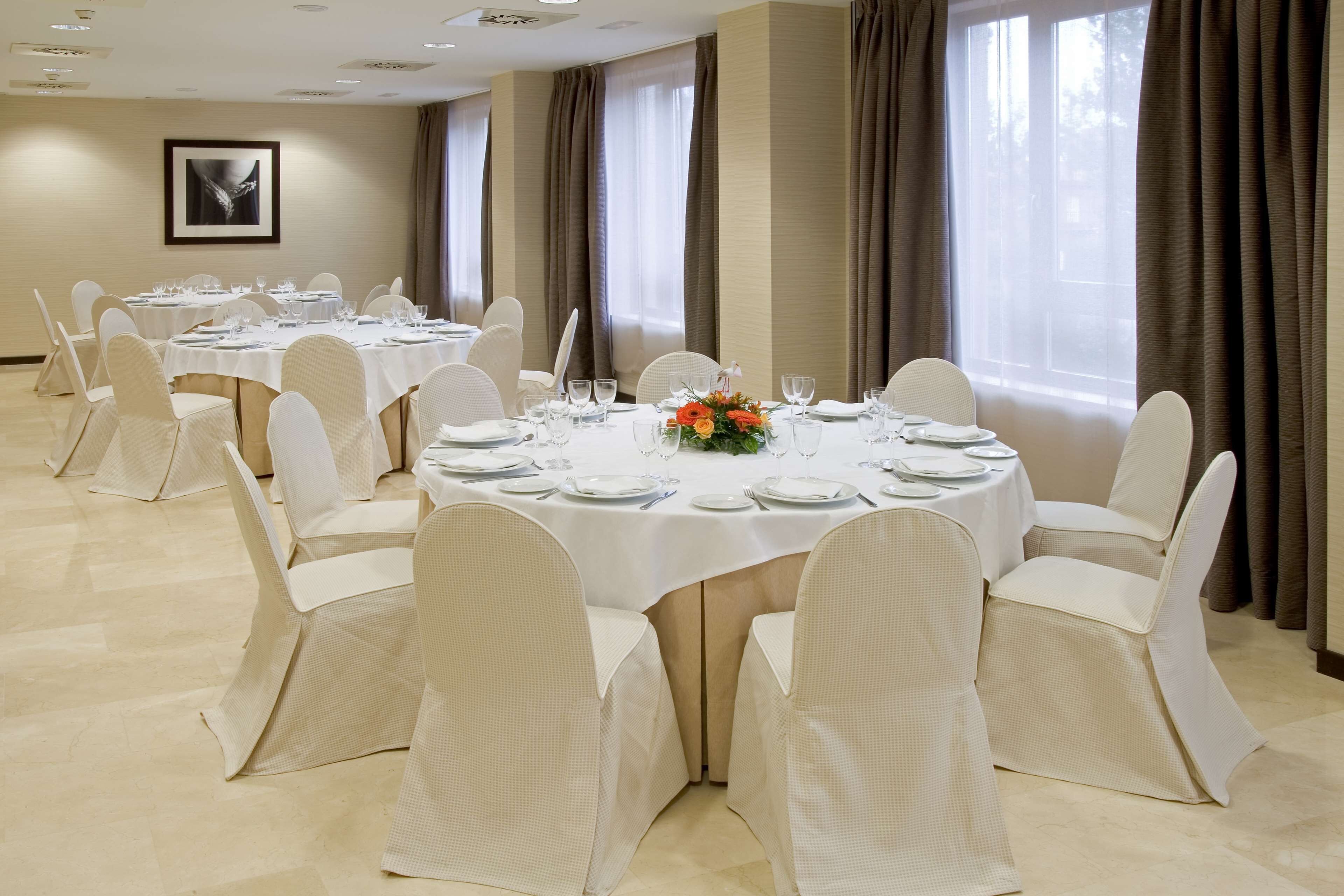 A conference room with round tables, white chairs, and a floral centerpiece.