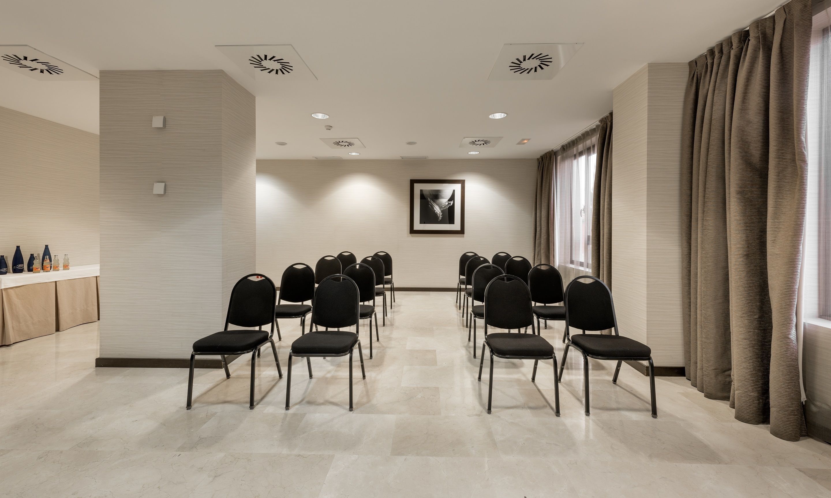 Un salón de conferencias con filas de sillas, una pizarra y un ventanal con cortinas.