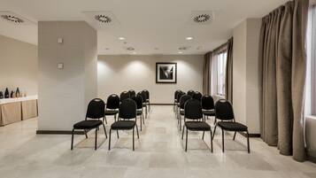 Un salón de conferencias con filas de sillas, una pizarra y un ventanal con cortinas.