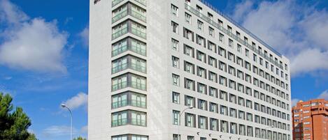 Um edifício moderno de hotel com um destaque para a placa "TH Hotel", diversas varandas e uma vista ampla do céu.