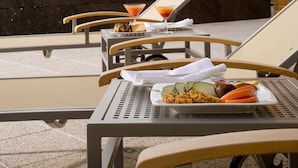 A rooftop terrace with lounge chairs, a table with a plate of food and a drink, and a view of a building and trees in the background. - NH Valladolid Bálago (Valladolid)